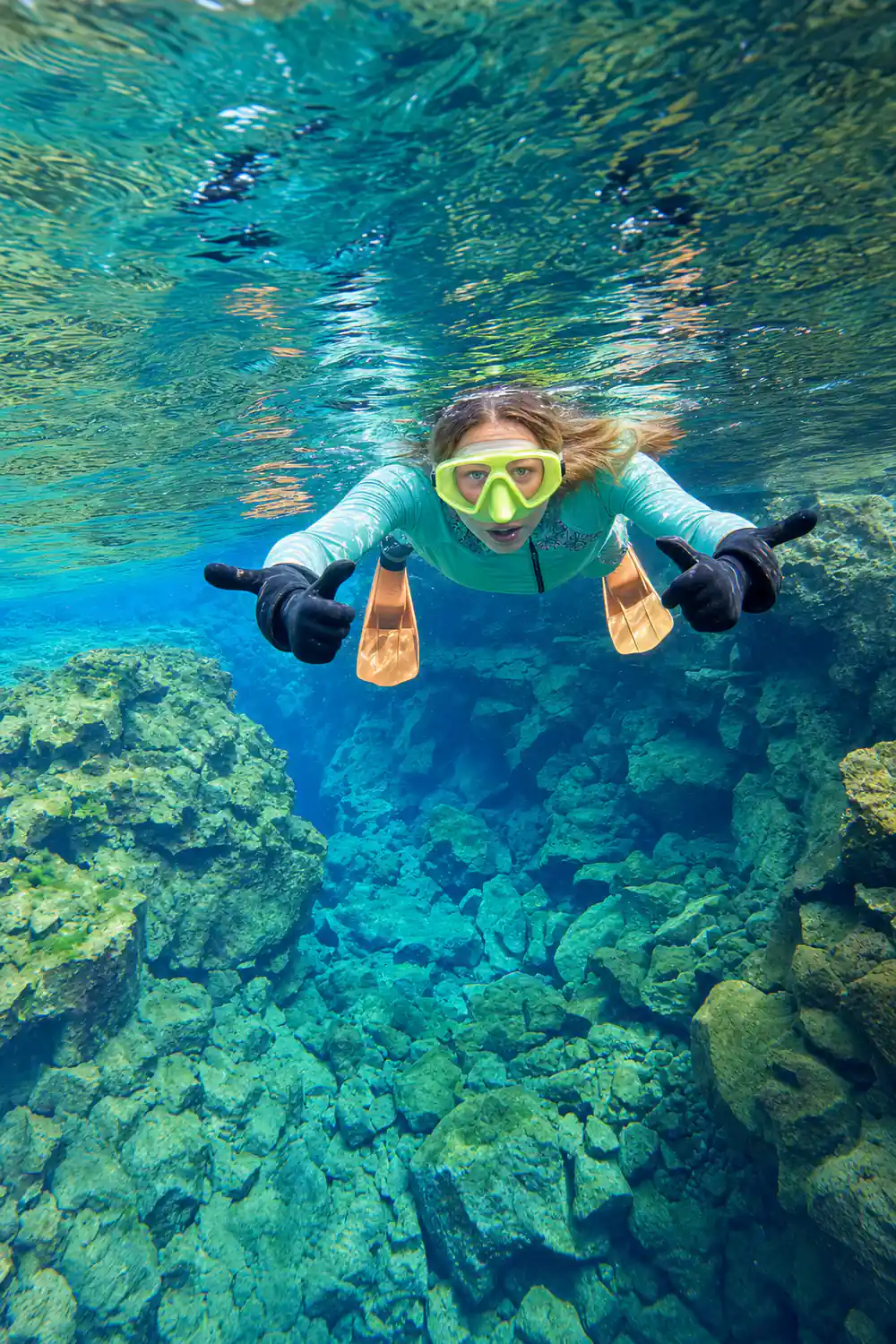 Diver with orange fins between green underwater rock formations