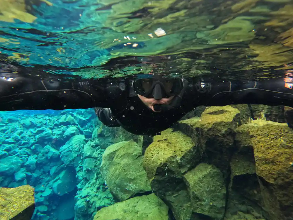 Diver posing horizontally underwater above bright green rocks