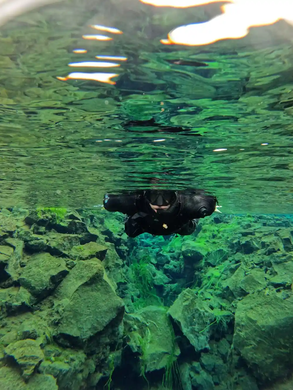 Diver swimming horizontally in green underwater cave passage