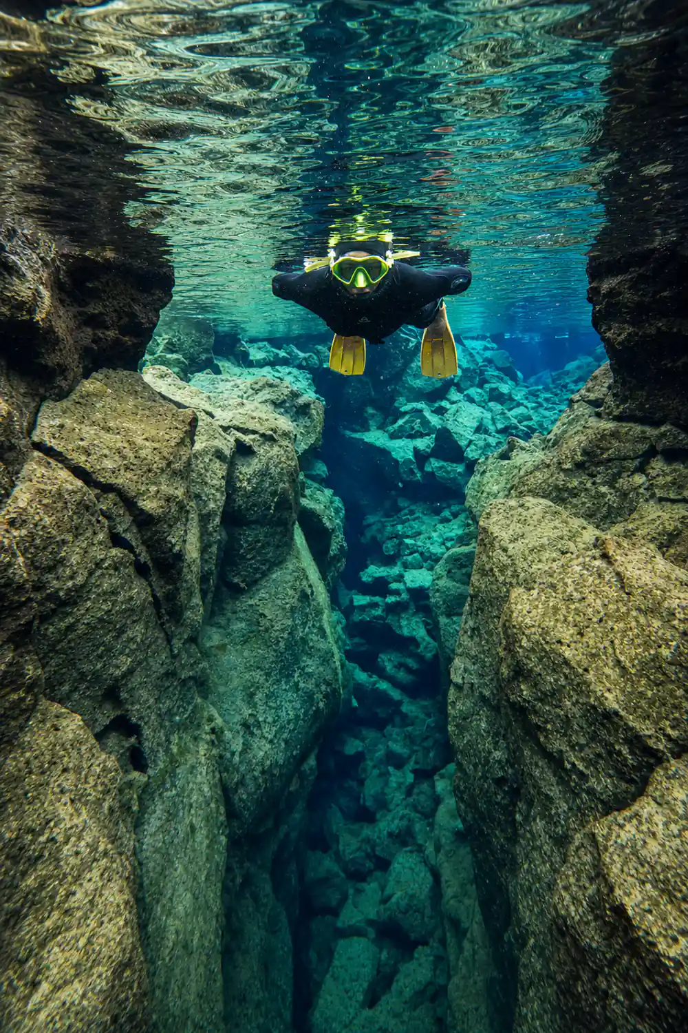 Diver swimming between moss-covered rock walls underwater