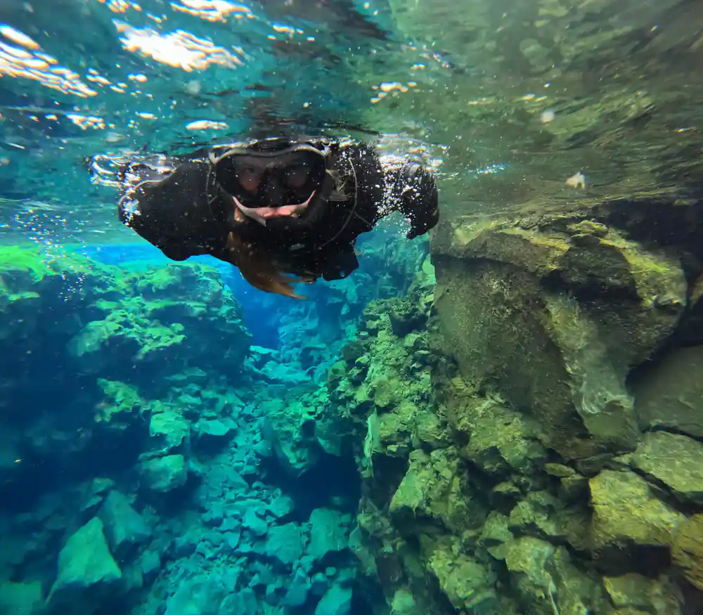 Diver swimming upward toward sunlit water surface near rocks