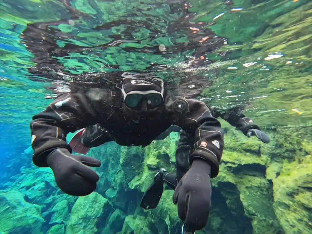 Diver underwater facing camera above green rocks