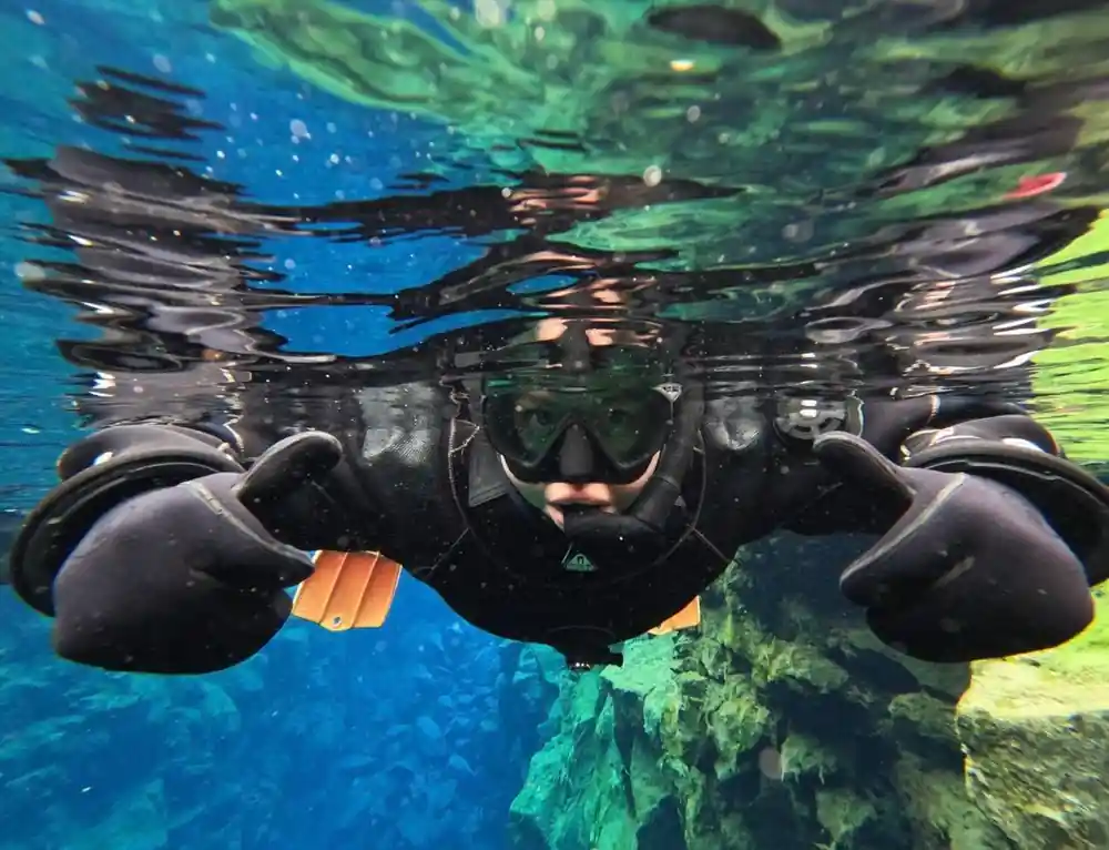 Diver underwater swimming above green and blue rocks