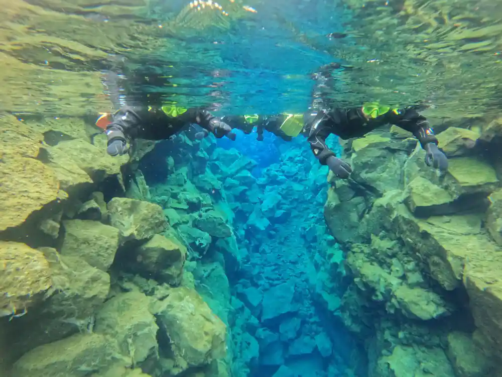 Divers in bright blue water between rocky walls