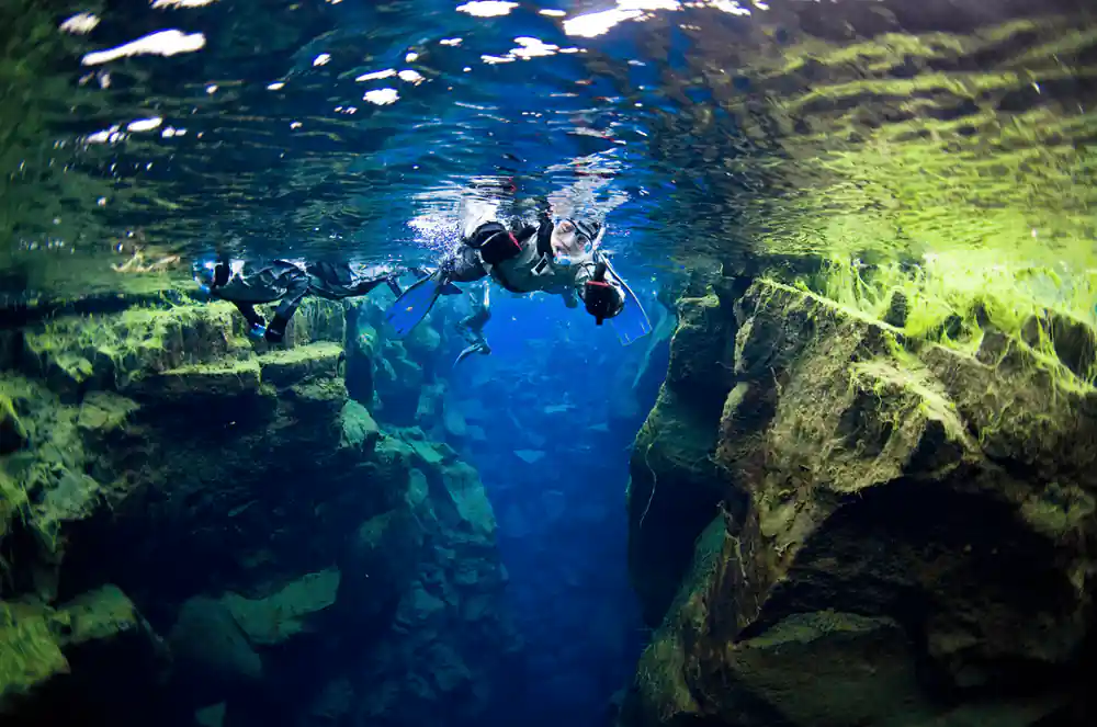 Divers swimming in cave with green-tinted rock walls