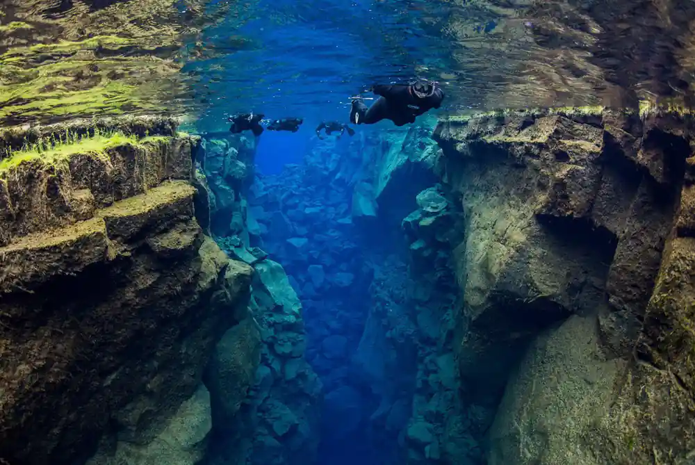 Divers swimming in green-lit underwater gorge with rock walls