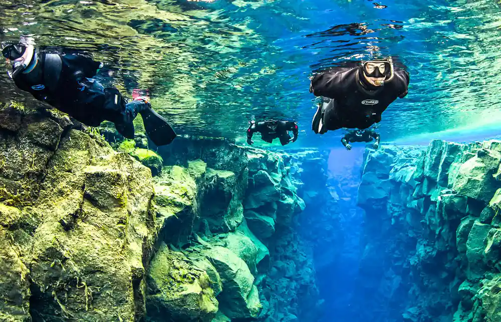 Multiple scuba divers exploring underwater rock formations
