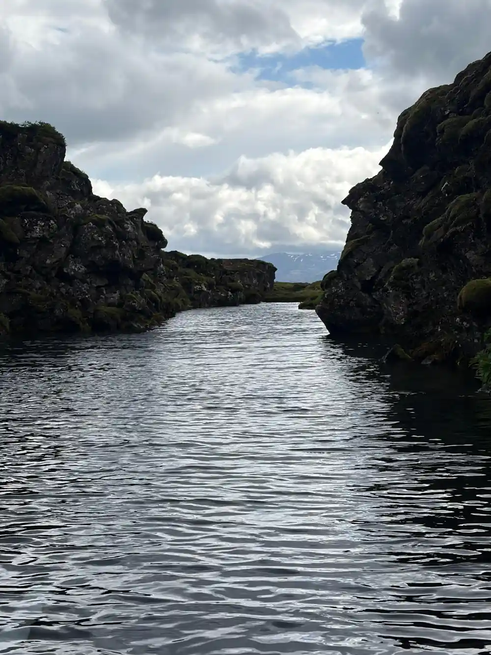 Narrow water channel between dark rocky outcrops under clouds