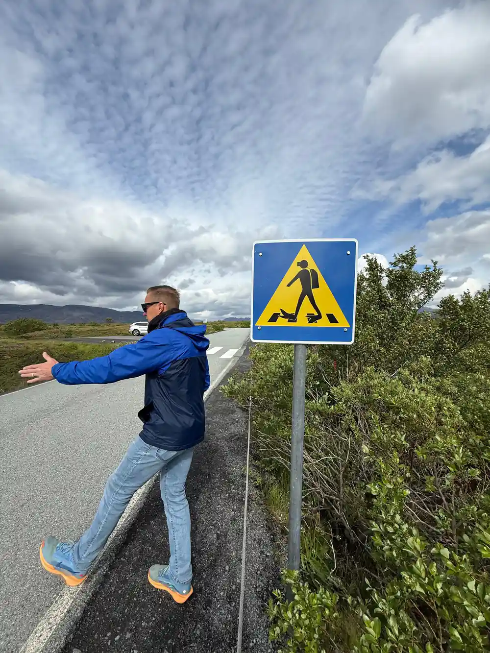 Person posing against yellow warning sign on roadside cliff