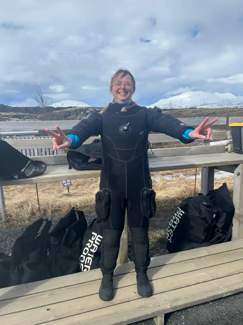 Person in wetsuit standing on wooden deck with arms outstretched