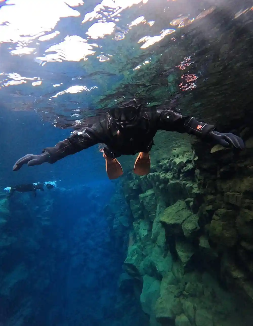 Scuba diver swimming near rocky underwater cliff face