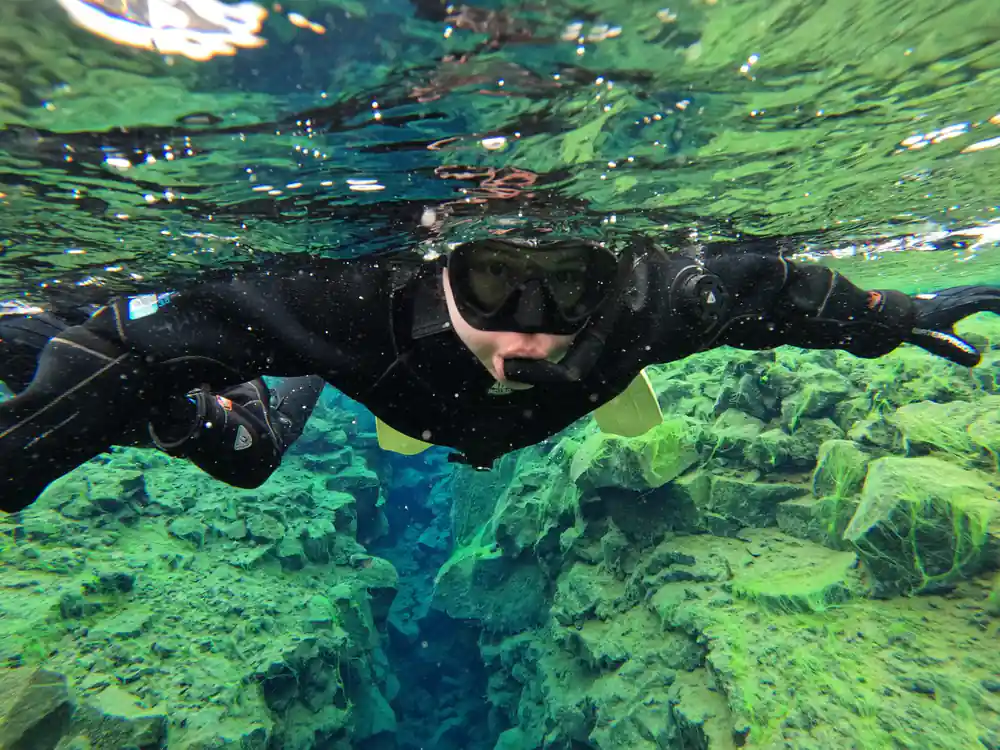 Snorkeler swimming over green and blue rocky seabed