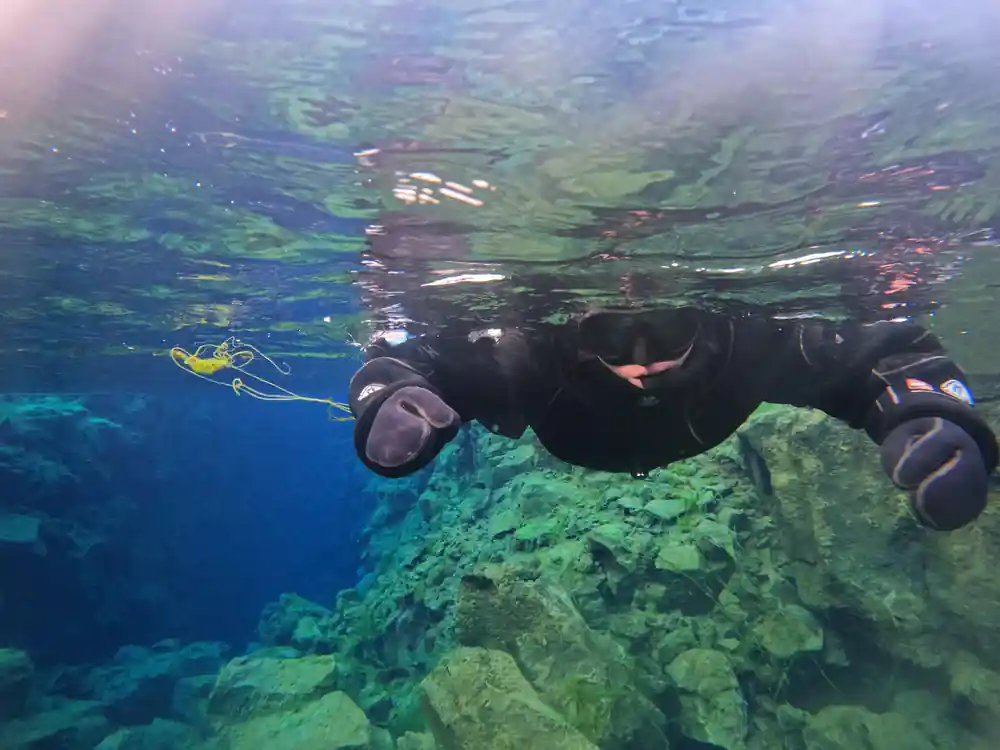 Snorkeler underwater swimming above green rocky terrain