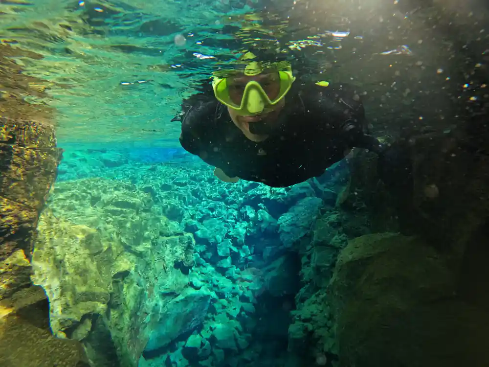 Snorkeler with yellow mask in clear turquoise water near rocks
