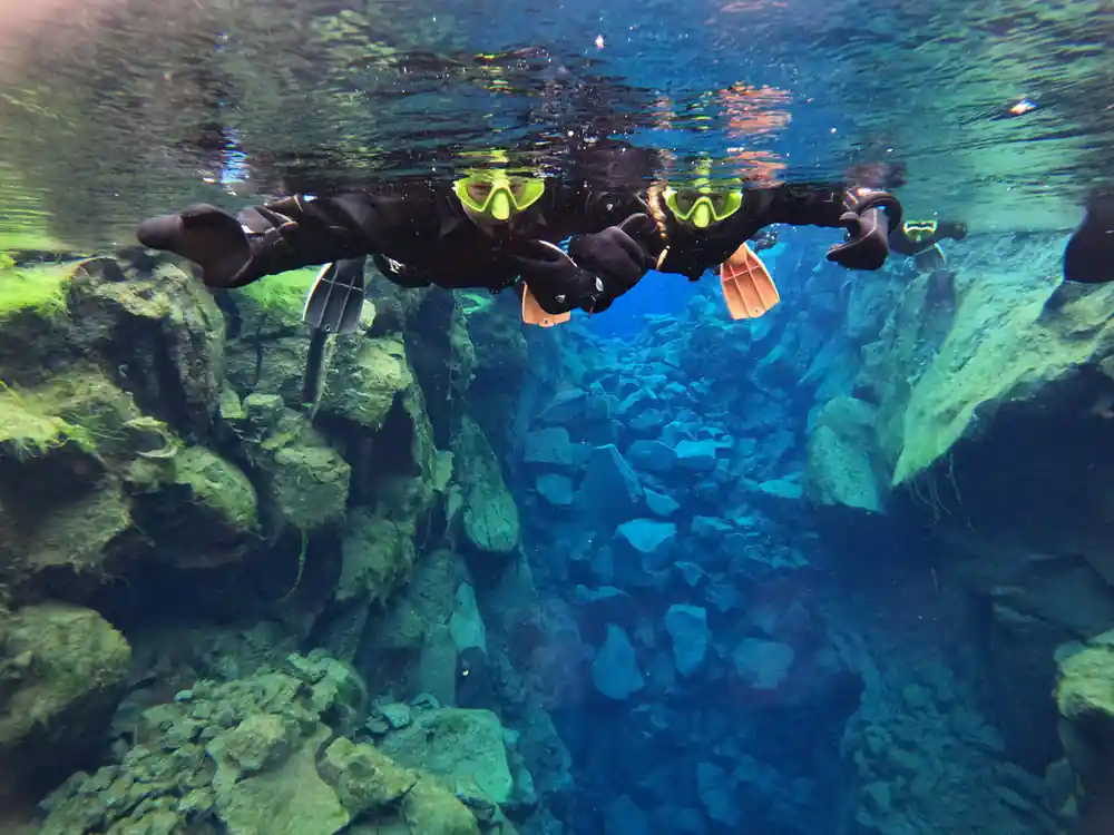 Three scuba divers swimming horizontally through clear blue water