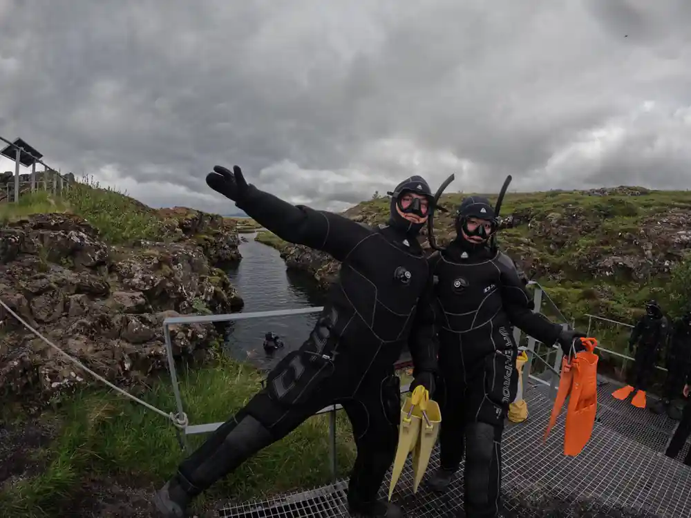 Two divers in wetsuits posing on platform with arm raised