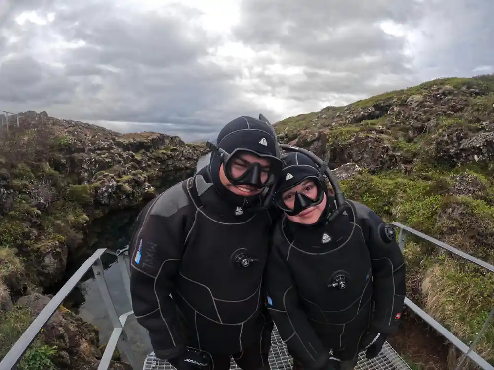 Two divers in wetsuits on rocky platform above water