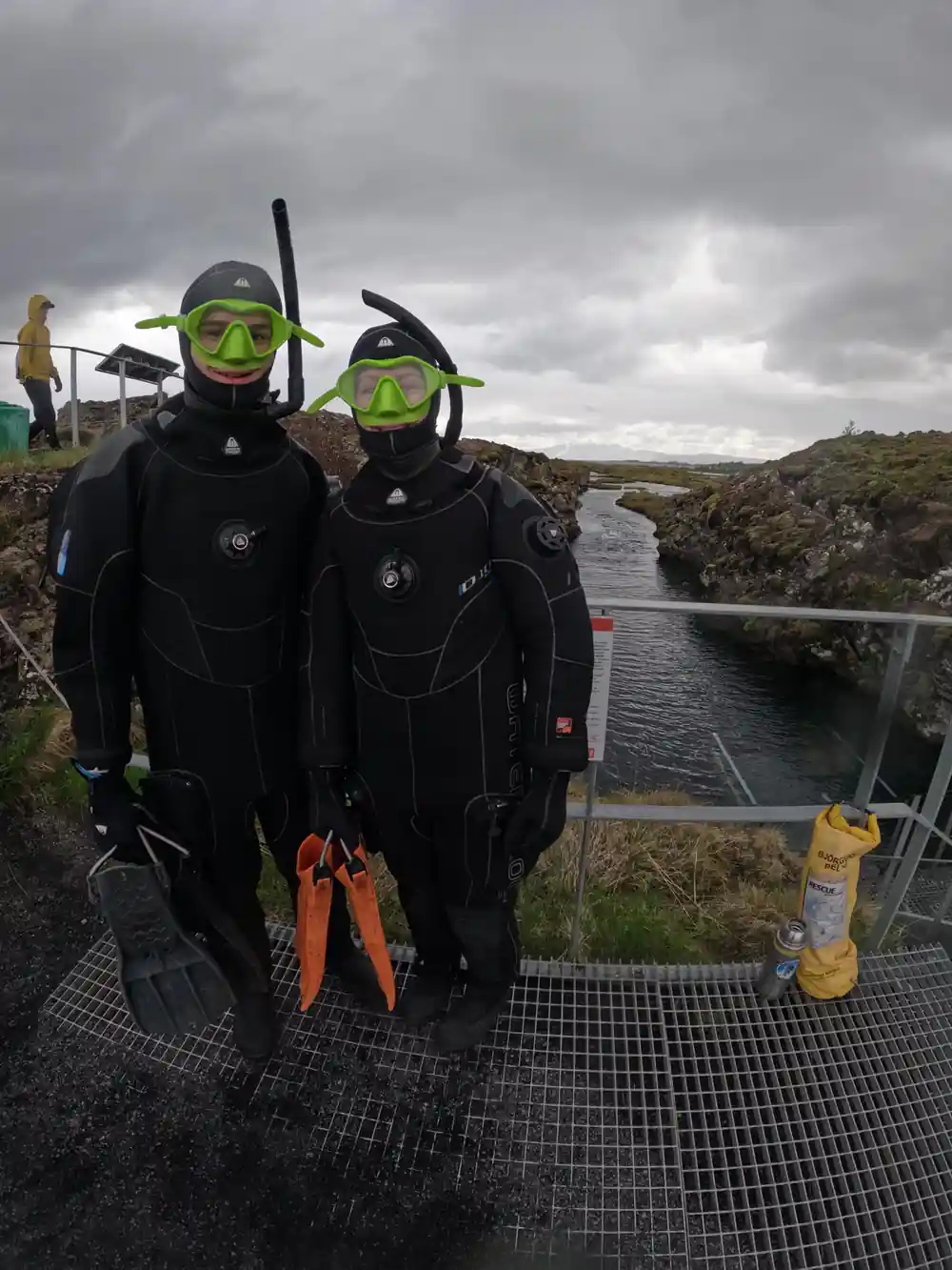 Two scuba divers in bright wetsuits by quarry pool