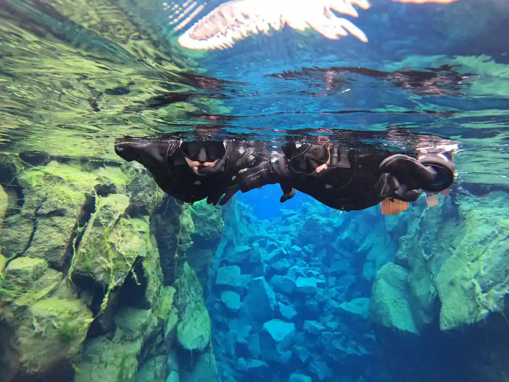 Two snorkelers swimming between green and blue rock formations