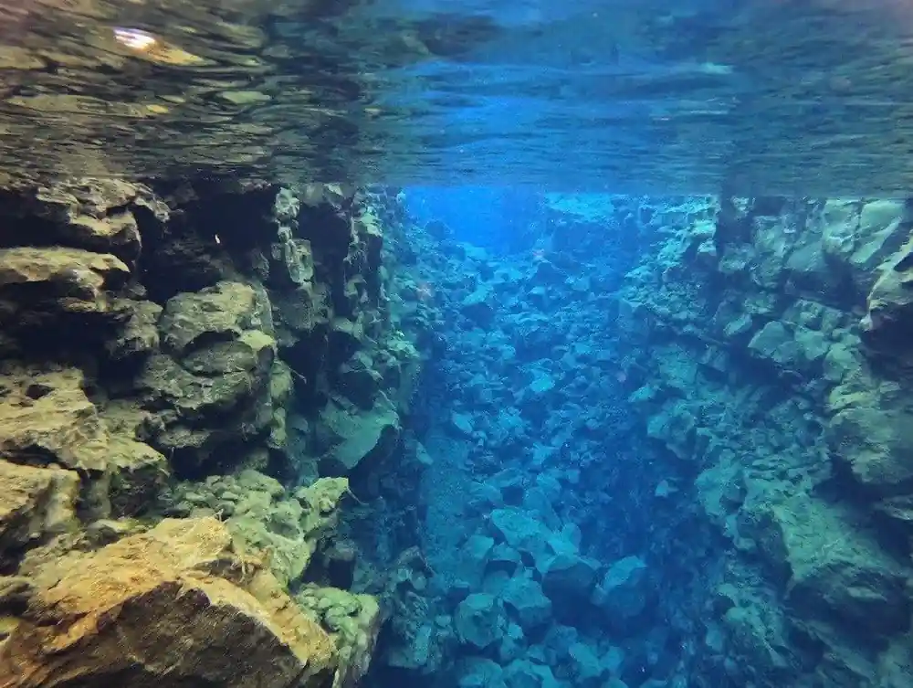 Underwater rocky cliff face with clear blue water